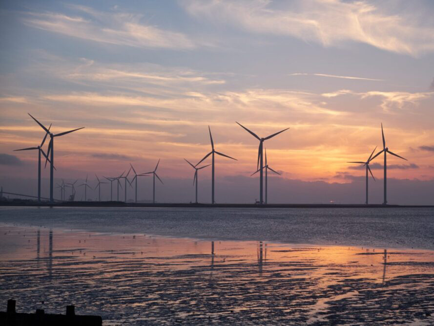 an image of a wind farm at sea as the sun is setting